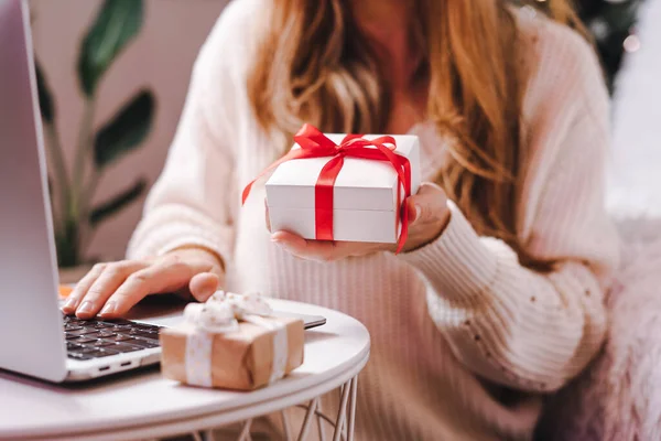 Woman holding gift typing at laptop. Holidays online shopping