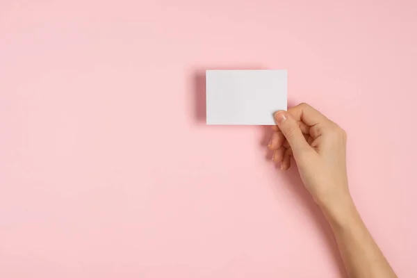 Manos de mujer sosteniendo tarjeta en blanco sobre mesa rosa — Foto de Stock