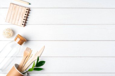 Cam kavanoz, yeşil yapraklar, defter ve geri dönüşümlü masa örtüsü manzarası. Sıfır atık, çevre dostu, doğal organik plastik konsept. Çatal bıçak takımı, toprak, beyaz ahşap üzerinde fotokopi alanı ile ayrıştırılabilir.