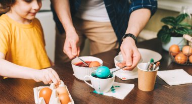 Paskalya günü. Baba ve oğul tahta arka planda yumurta boyuyor. Aile mutfakta oturuyor. Paskalya hazırlığı, yaratıcı ev yapımı dekorasyon