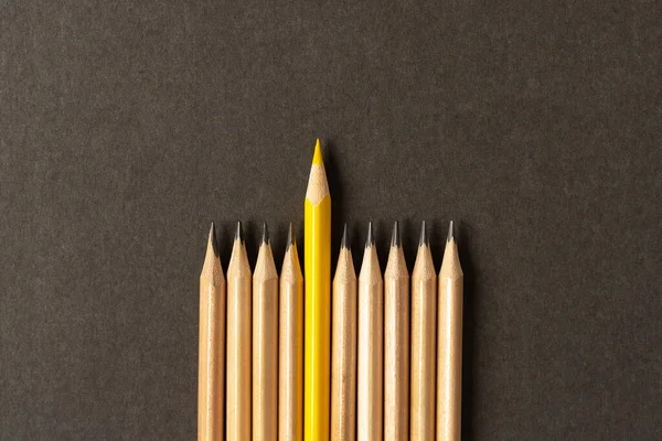 One yellow pencil standing out from the series of gray pencils.