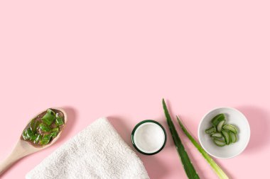 Aloe vera suyu, organik krema, jöle, havlu ve yeşil yapraklı üst manzara..