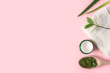 Aloe vera suyu, organik krema, jöle, havlu ve yeşil yapraklı üst manzara..