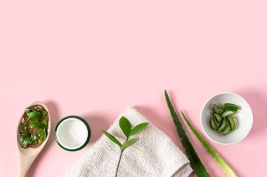 Aloe vera suyu, organik krema, jöle, havlu ve yeşil yapraklı üst manzara..