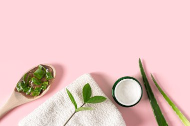 Aloe vera suyu, organik krema, jöle, havlu ve yeşil yapraklı üst manzara..
