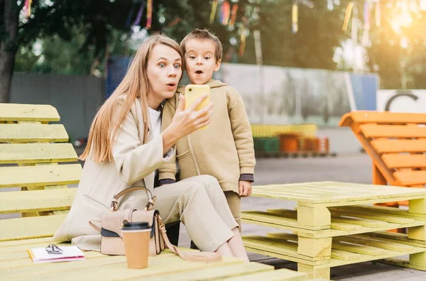 Drôle et surpris jeune maman avec préscolaire fils assis sur banc — Photo