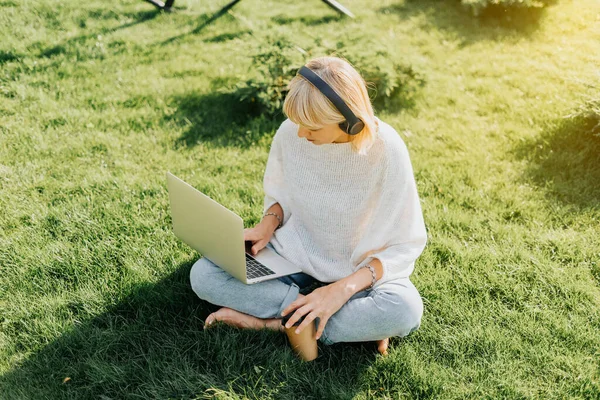 Çimlerin üzerinde oturan dizüstü bilgisayar kullanan kadın. — Stok fotoğraf