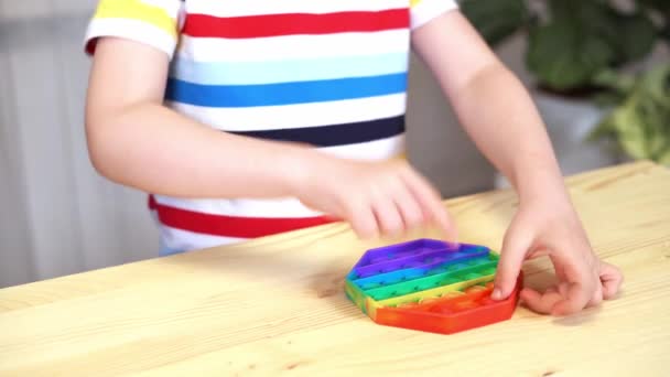 Close up of Kid fingers playing with the Pop It fidget. Empurre a bolha pop brinquedo sensorial fidget flexível em mãos de crianças. Alívio de estresse de silício. Conceito de saúde mental. Foco seletivo no brinquedo — Vídeo de Stock