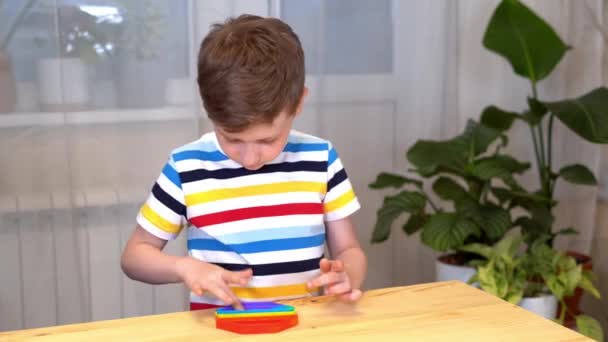 Primer plano de Kid dedos jugando con el Pop It fidget. Empuje la burbuja pop flexible fidget juguete sensorial en las manos de los niños. Alivio de estrés de silicio. Concepto de salud mental. Enfoque selectivo en el juguete — Vídeo de stock