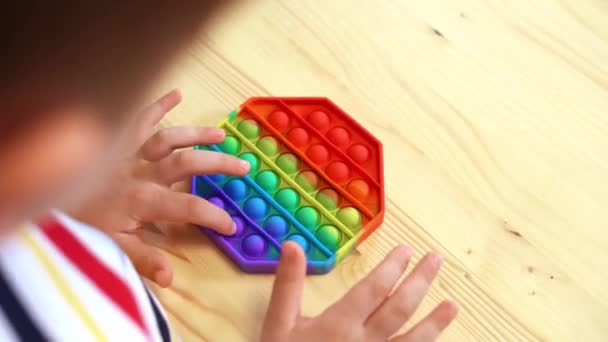 Primer plano de Kid dedos jugando con el Pop It fidget. Empuje la burbuja pop flexible fidget juguete sensorial en las manos de los niños. Alivio de estrés de silicio. Concepto de salud mental. Enfoque selectivo en el juguete — Vídeo de stock
