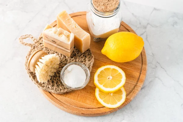 Eco friendly natural cleaners, jar with baking soda, dish brush, lemon, soap on white marble table background. Organic ingredients for homemade cleaning. Zero waste concept