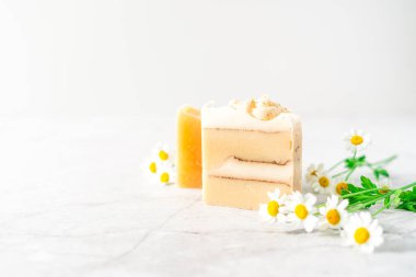 Beyaz mermer arka planda papatya çiçekli ev yapımı bitkisel sabun. Sıfır atık, doğal organik banyo kozmetikleri. Plastiksiz hayat. Ekolojik cilt bakımı, vücut tedavisi konsepti.