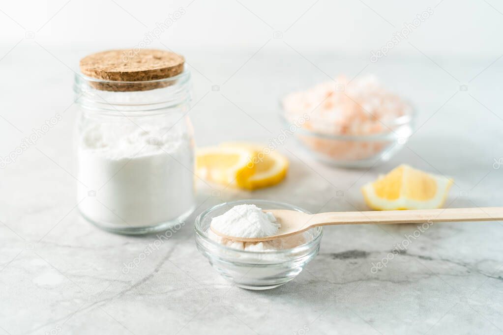 Eco friendly natural cleaners, jar with baking soda, lemon, pink salt and wooden spoon on marble table background. Organic ingredients for homemade cleaning. Zero waste concept