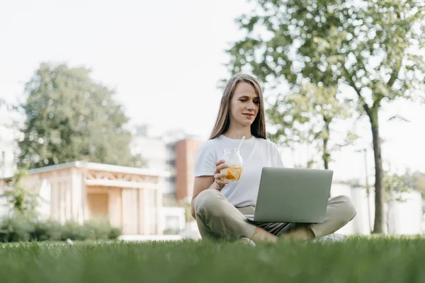 Dizüstü bilgisayarlı bir kadın çimlerin üzerinde oturuyor. — Stok fotoğraf