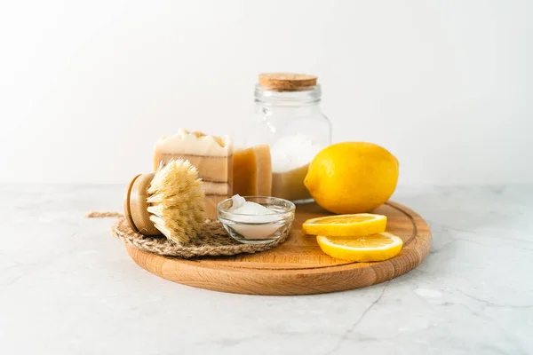 Eco friendly natural cleaners, jar with baking soda, dish brush, lemon, soap on white marble table background. Organic ingredients for homemade cleaning. Zero waste concept