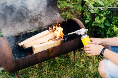 Yakından adam balonla gaz ocağını tutuyor ve ızgarada ateş yakıyor. Arka bahçedeki yeşil çimlerin üzerinde alev tabancası var. Erkekler ateş yakar