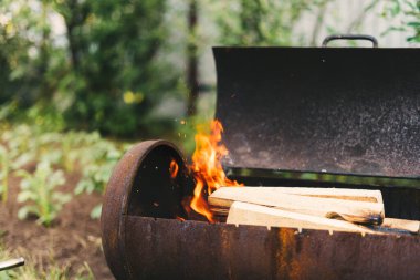 Izgarada barbekü için ateş yakıyorum. Arka bahçedeki yeşil çimlerin arka planında alevler var. Ateş yak.