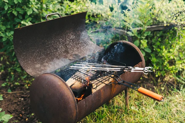 Rozdělat oheň v grilu na grilování. Plamen na pozadí zelené trávy ve večerních hodinách na dvoře. Zapal oheň — Stock fotografie