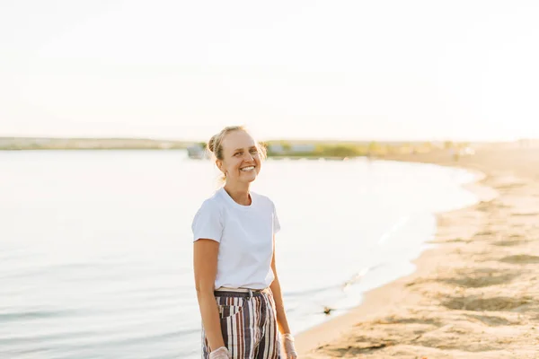 Junge attraktive lächelnde blonde Frau am Strand, die freudig in die Kamera blickt, mit Meer im Hintergrund. Wandern auf Sand am Meer — Stockfoto