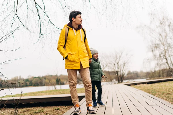 Ojciec w żółtym płaszczu i syn bawiący się w lesie. Szczęśliwa rodzina z dzieckiem chłopiec zabawy i zabawy na świeżym powietrzu na tle jesiennego parku — Zdjęcie stockowe