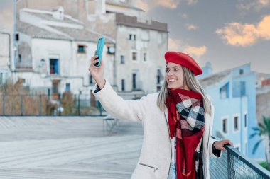 Gün batımında cep telefonuyla fotoğraf çeken genç bir kadın..