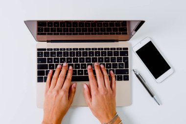 Bir kadının elleri dizüstü bilgisayarda, bir kalem ve cep telefonunun yanında yazıyor..