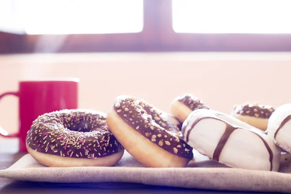 Donuts diferentes em uma mesa de madeira e uma caneca vermelha de sagacidade café quente — Fotografia de Stock