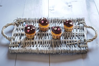 Four delicious chocolate cupcakes on a wicker tray clipart