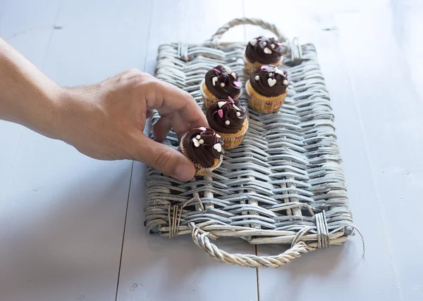 Hand att sätta en läcker choklad cupcakes på en wicker bricka — Stockfoto