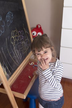 Little girl scribbling on drawing of flowers on blackboard clipart