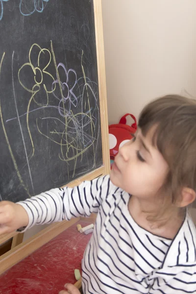 Little girl painting flowers on blackboard — Stock Photo, Image