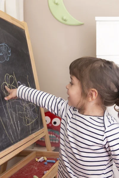 Little girl point at her drawing of flowers on blackboard — Stock Photo, Image