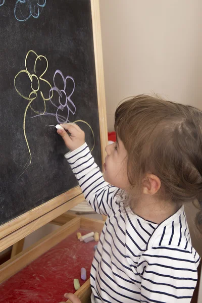 Little girl painting flowers on blackboard — Stock Photo, Image
