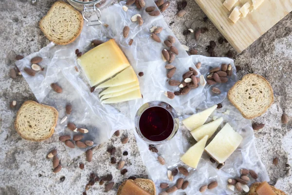 Rött vin glas tillsammans med utbud av ostar, rostad mandel och rostat bröd Royaltyfria Stockbilder