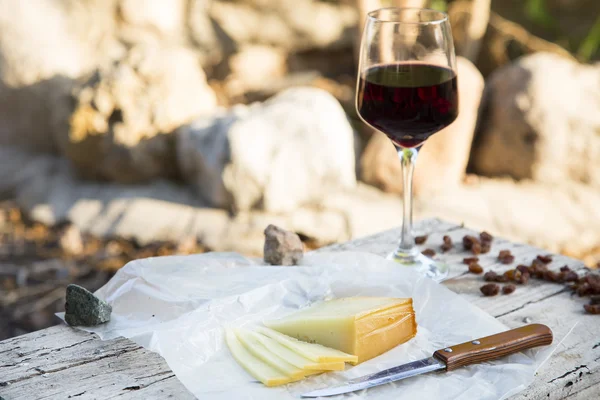 Morceaux de fromage et raisins secs avec un verre de vin rouge sur un vieux bois — Photo