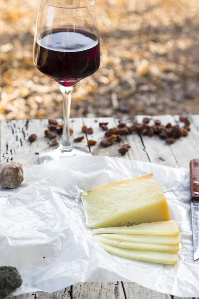 Morceaux de fromage et raisins secs avec un verre de vin rouge sur une vieille table en bois — Photo