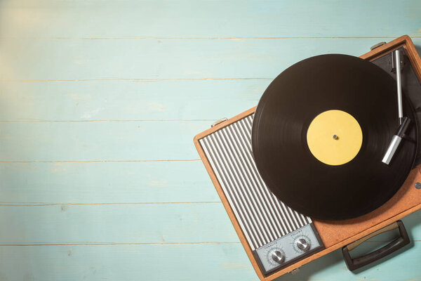 Vintage gramophone with a vinyl record on green wooden table, top view and copy space.