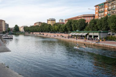 Milan, İtalya-Eylül 29,2020: İnsanlar Naviglio Milano kanalı boyunca yürüyor ve Coronavirus salgını sırasında barlarda dinleniyor (Covid-19) Darsena bölgesi, su üzerinde kano sporu yapan diğer insanlar.