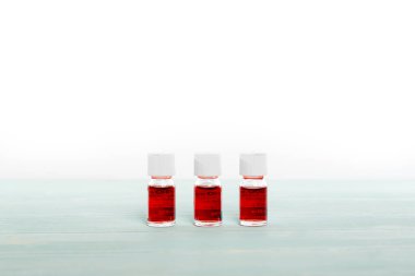 Kırmızı sıvıyla dolu üç ilaç şişesi beyaz arkaplanda sıraya dizilmiş.