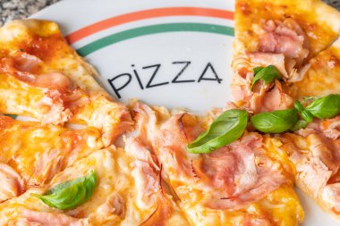 Tabakta peynirli taze İtalyan pizzası (mozzarella), domates, jambon ve küçük taze fesleğen yaprakları yazılı pizza..