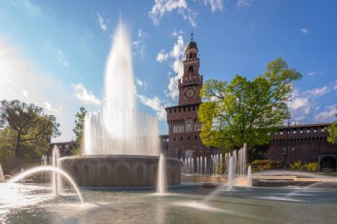 Sforza Kalesi 'nin ana girişi - Sforzesco şatosu ve önündeki çeşme, uzun pozlu fotoğraf, güneşli gün ve gökyüzünde bulutlar, Milan, İtalya
