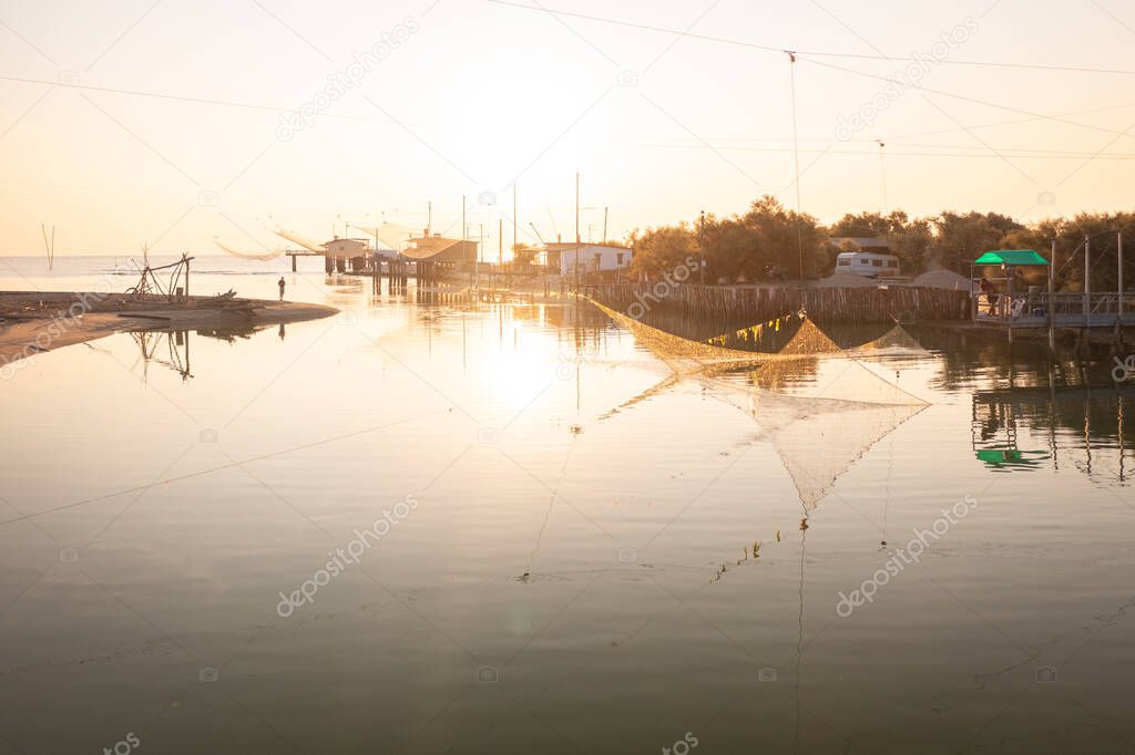 Panorama view of fishing huts on river at sunrise with typical italian fishing machine, called 