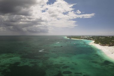 Güneşli bir günde tropikal deniz kıyısında kumlu bir sahil manzarası. Hint Okyanusu 'nda yaz tatili, Zanzibar, Afrika. Tekneli manzara, yeşil ağaçlar, şeffaf turkuaz su.