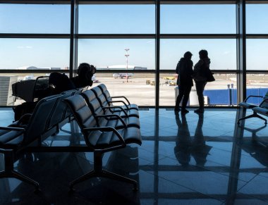 Havaalanındaki yolcuların siluetleri havaalanı ve uçak pistinin arka planındaki bekleme salonunda..