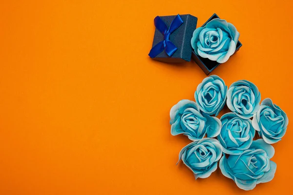 Blue rose flowers with a rose flower in a blue gift box on an orange background