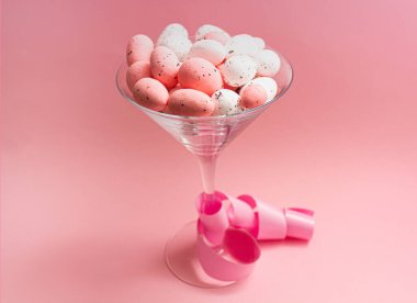 Pembe ve beyaz Paskalya yumurtaları ve pembe arka planda bir bardak şarap. Bahar tatili kavramı