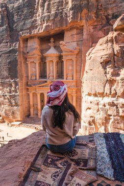 Genç Asyalı gezgin Hazine 'nin önündeki kayanın üzerinde ya da Petra harabelerinde El-Hazine' de ve antik Nabatean şehri Ürdün, Arap, Asya 'da oturuyor.