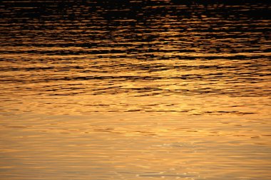 Gün batımı göletteki suda parlıyor.