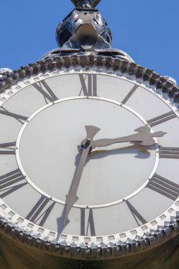 Parktaki bir sokak saatinin metal kadranı ve sandalyeleri