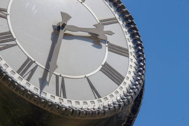 Parktaki bir sokak saatinin metal kadranı ve sandalyeleri